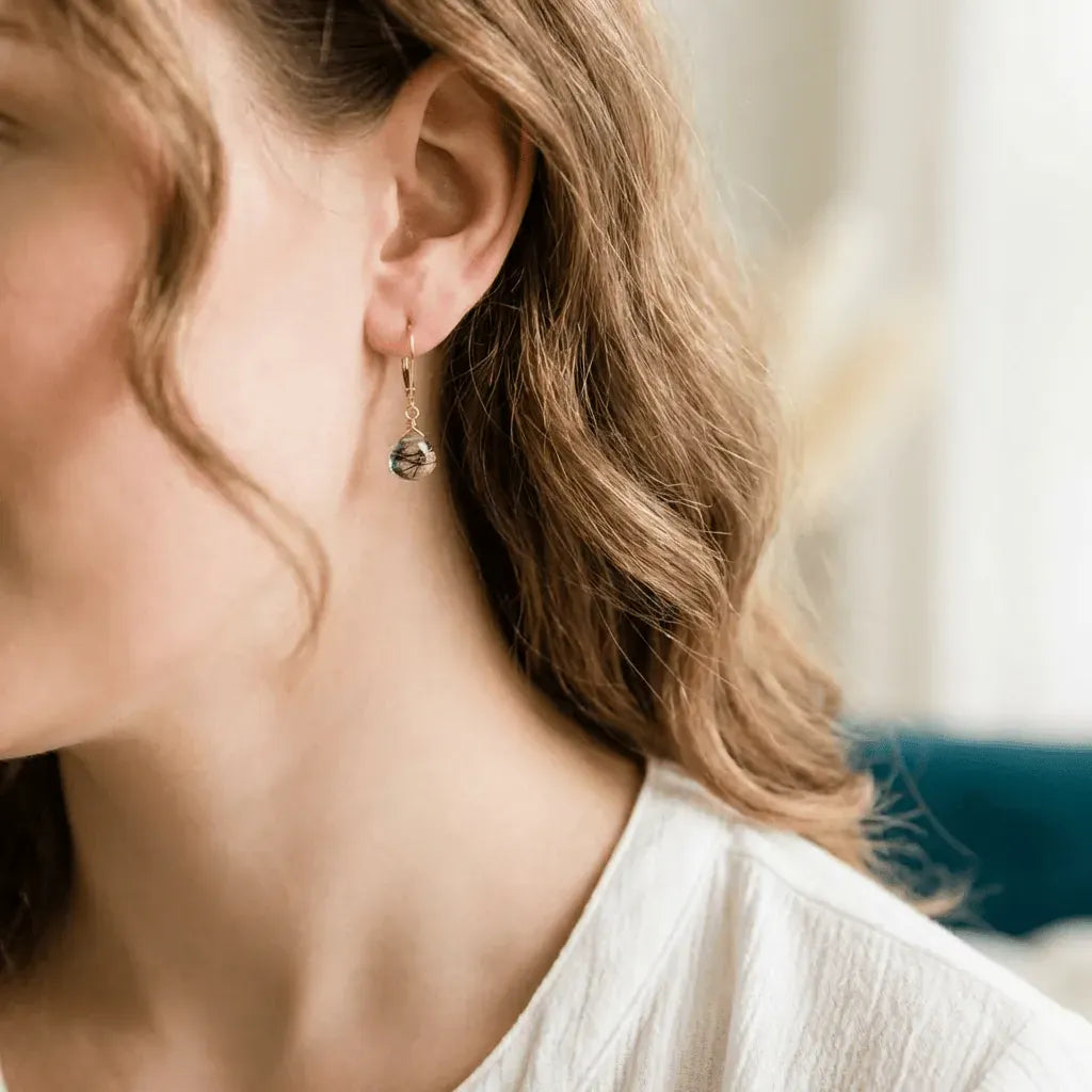 Close-up of a person wearing a gold earring with a dark gemstone.