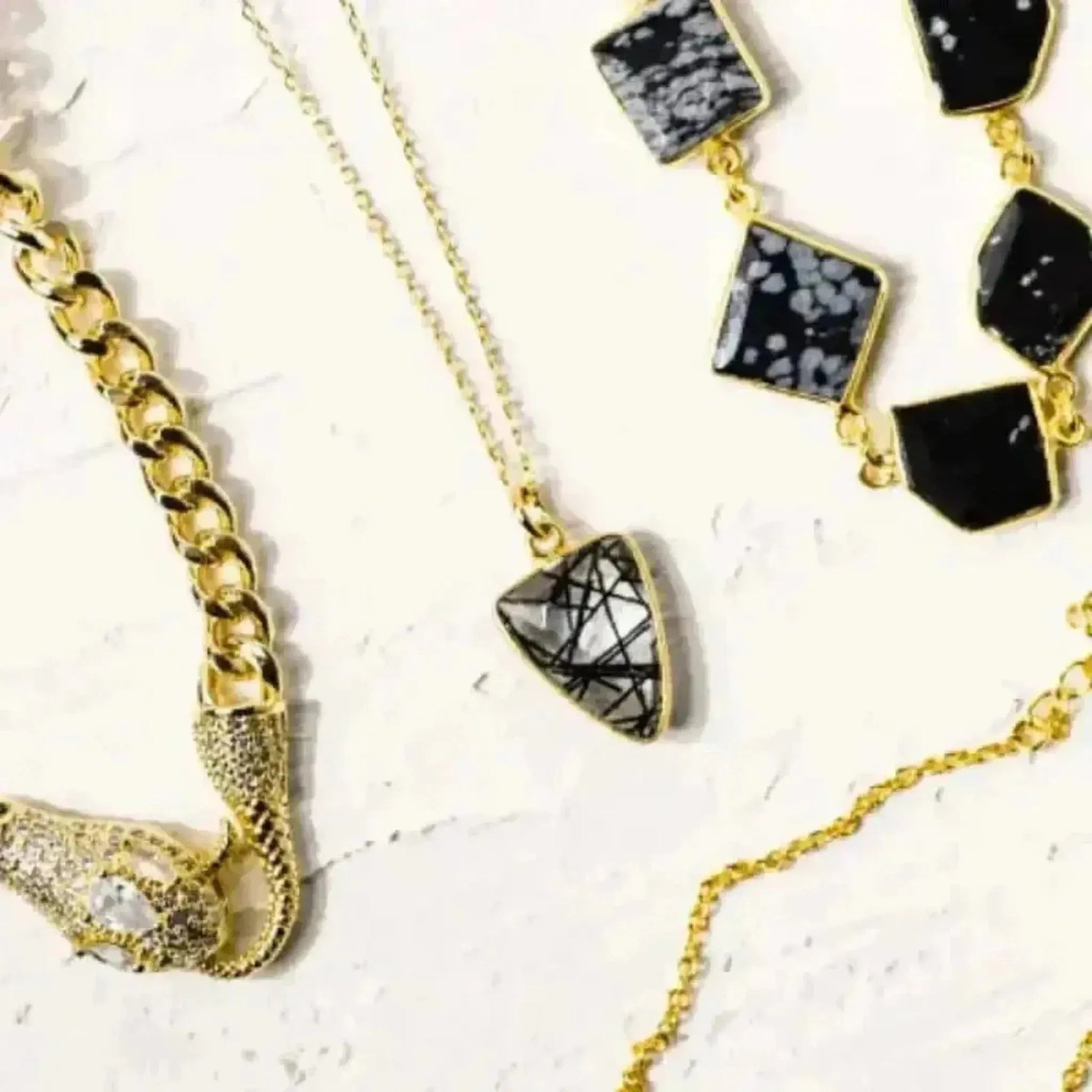 A collection of jewelry featuring a gold-plated chain necklace with a rutilated quartz gemstone pendant, along with other gemstone earrings and pendants.