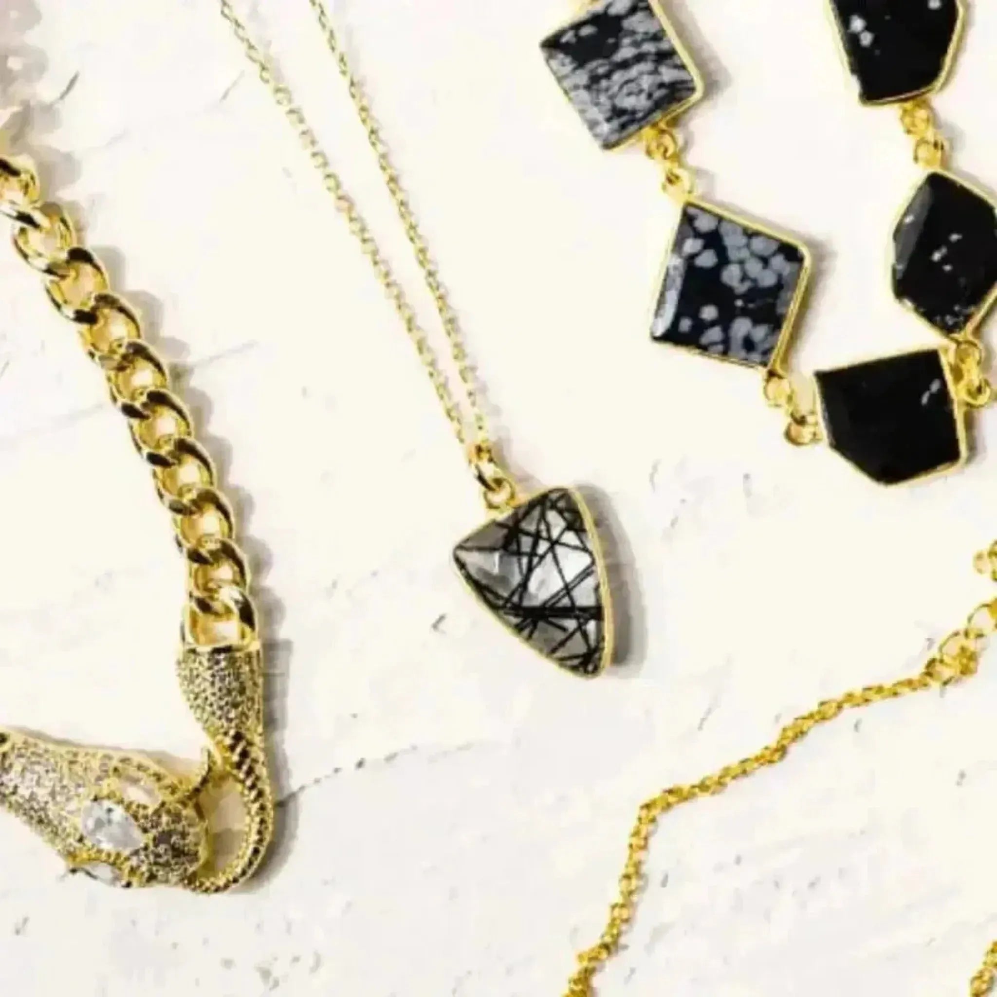 A collection of jewelry featuring a gold-plated chain necklace with a rutilated quartz gemstone pendant, along with other gemstone earrings and pendants.