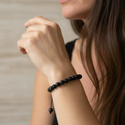 Close-up of a person wearing a black beaded bracelet on a neutral background
