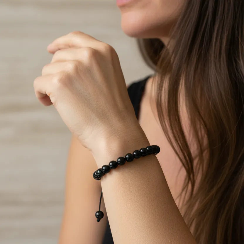 Close-up of a person wearing a black beaded bracelet on a neutral background