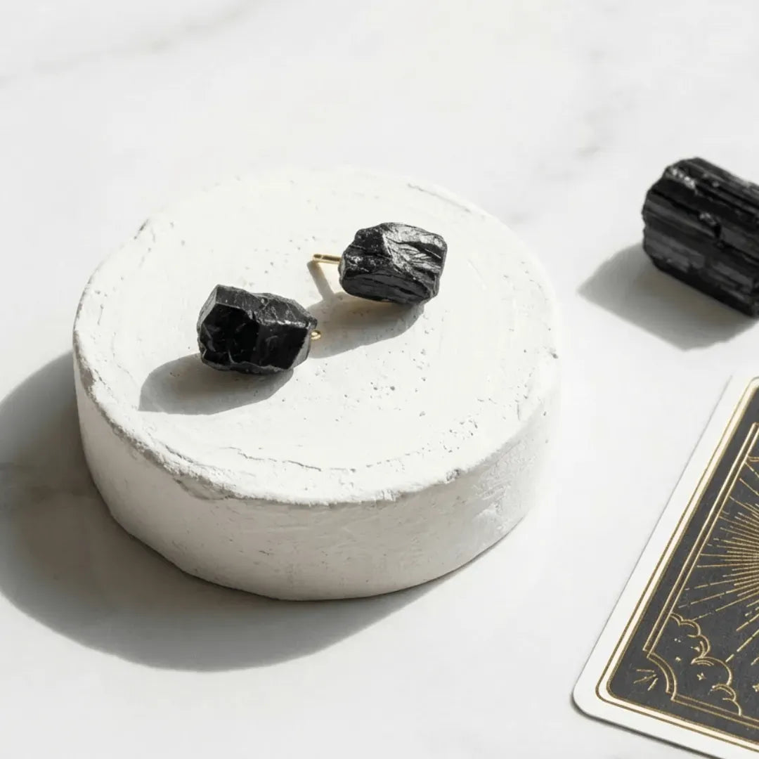 Black stone earrings on a white pedestal with a playing card in the background