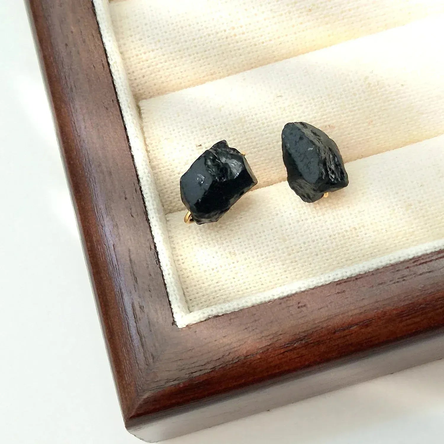 Two black gemstones on a white cushion inside a wooden display box.