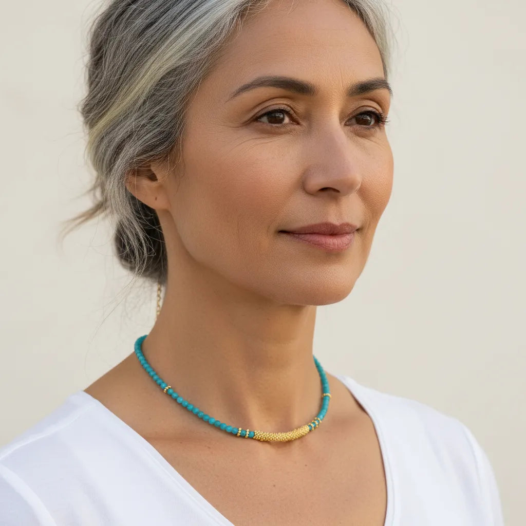 Woman wearing a turquoise beaded necklace against a plain background