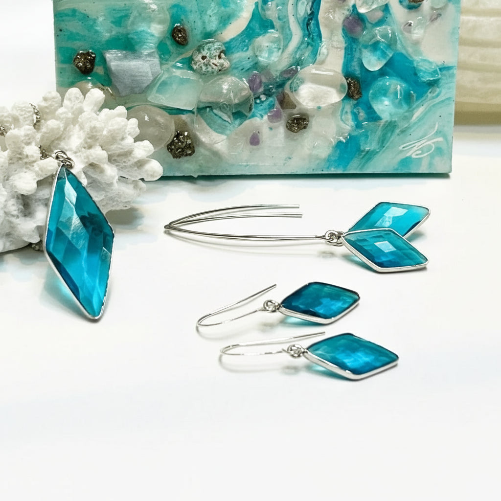 Blue square earrings with silver hooks on a white surface, with a decorative blue and white background.