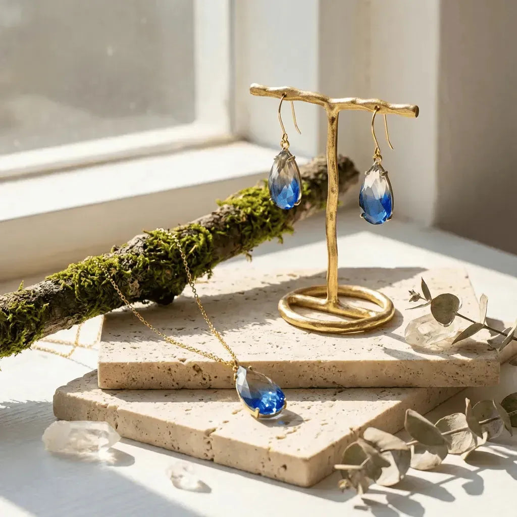 Gold necklace and blue teardrop earrings on a gold stand with a natural background