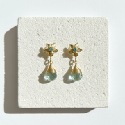 A pair of gold-toned dangle earrings with light blue jellyfish charms and faceted pale green beads