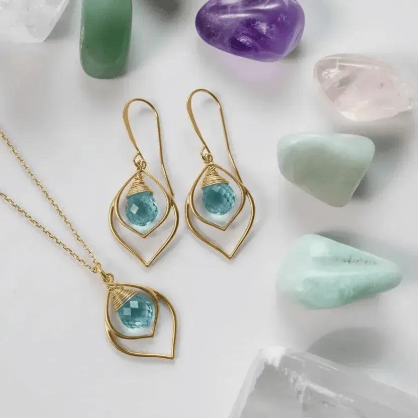 Gold earrings with blue gemstones on a white surface with crystals.