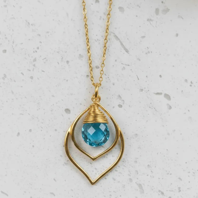 Gold necklace with a blue pendant on a light gray background