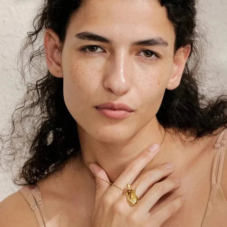 Woman wearing a gold necklace and ring against a neutral background