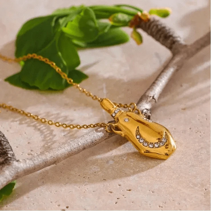 Gold necklace with a pendant on a textured surface with green leaves