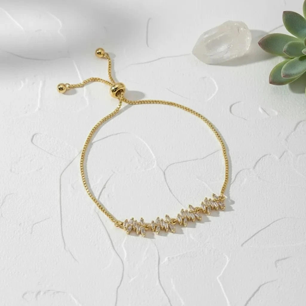 Gold bracelet with small beads on a white surface with a succulent plant