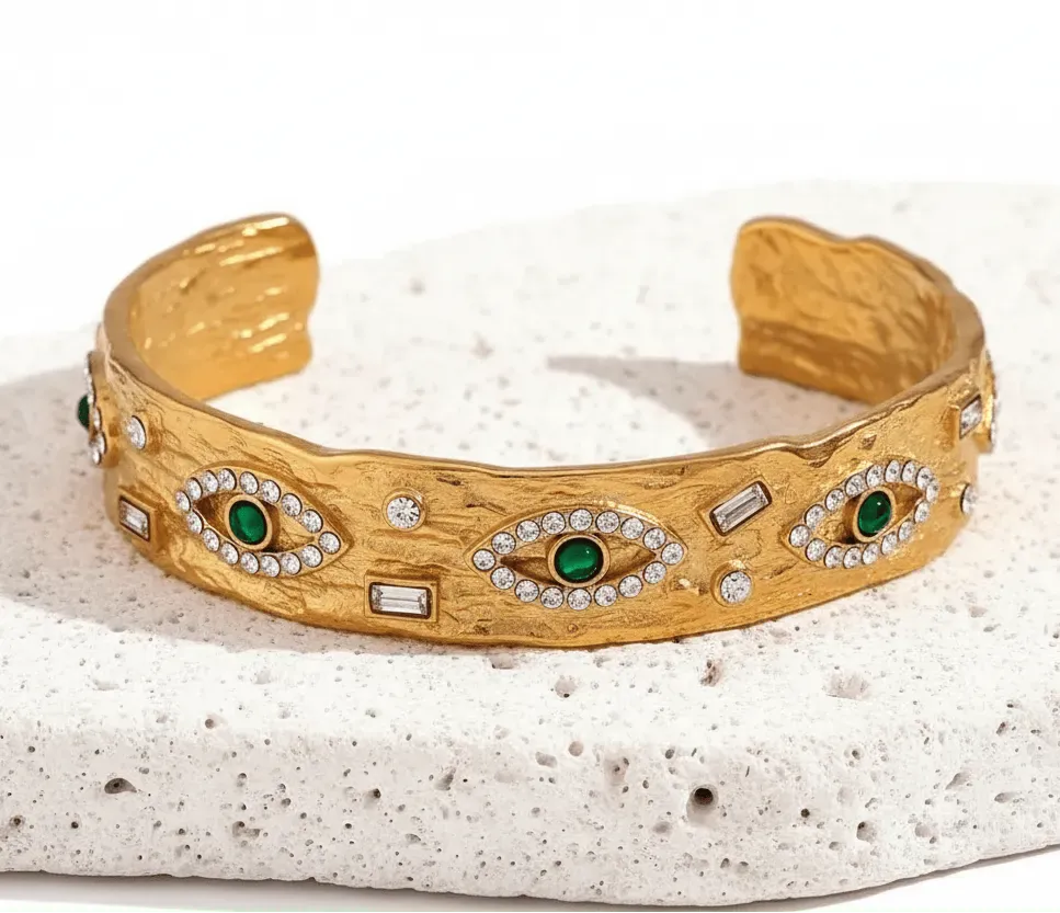 Gold bracelet with green gemstones and white stones on a textured white surface