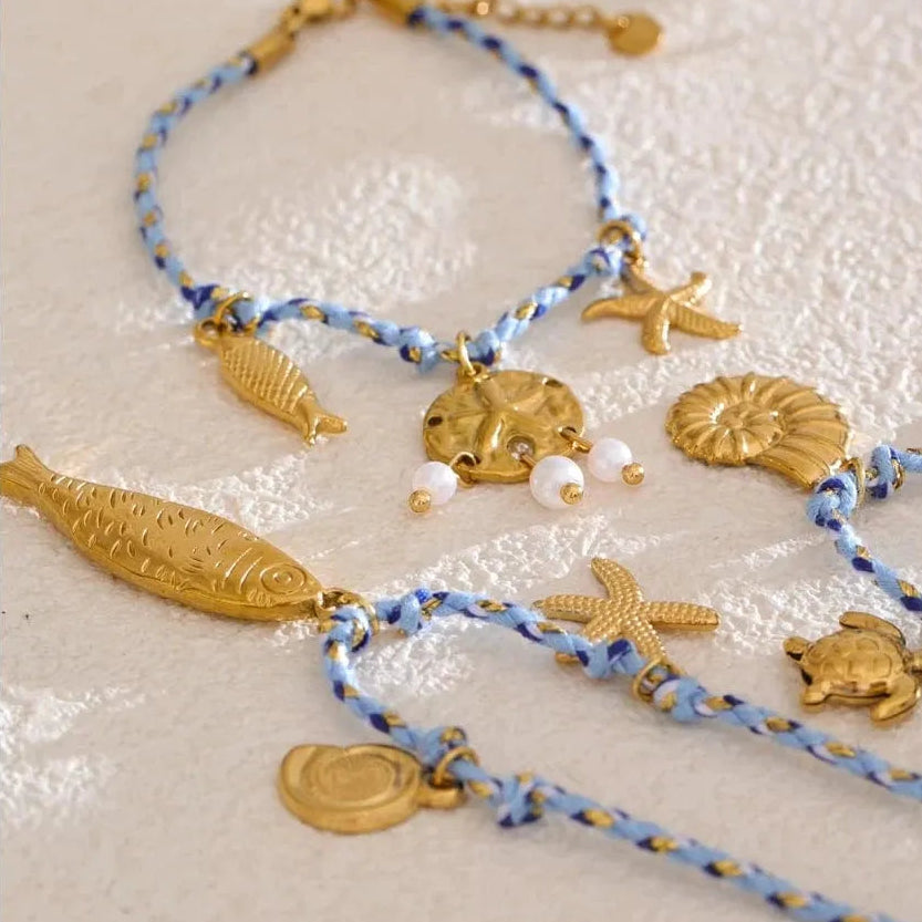 Set of gold and blue beaded bracelets with starfish, shell, and fish charms on a textured beige surface.