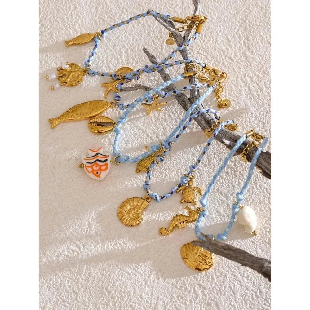 Gold and blue bracelets with sea-themed charms on a textured beige surface