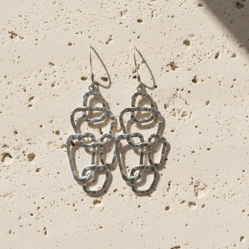 Silver chain-style earrings on a textured fabric background