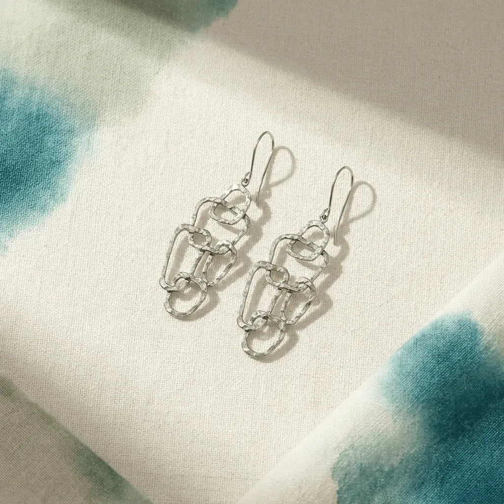Silver chain-link earrings on a textured fabric background