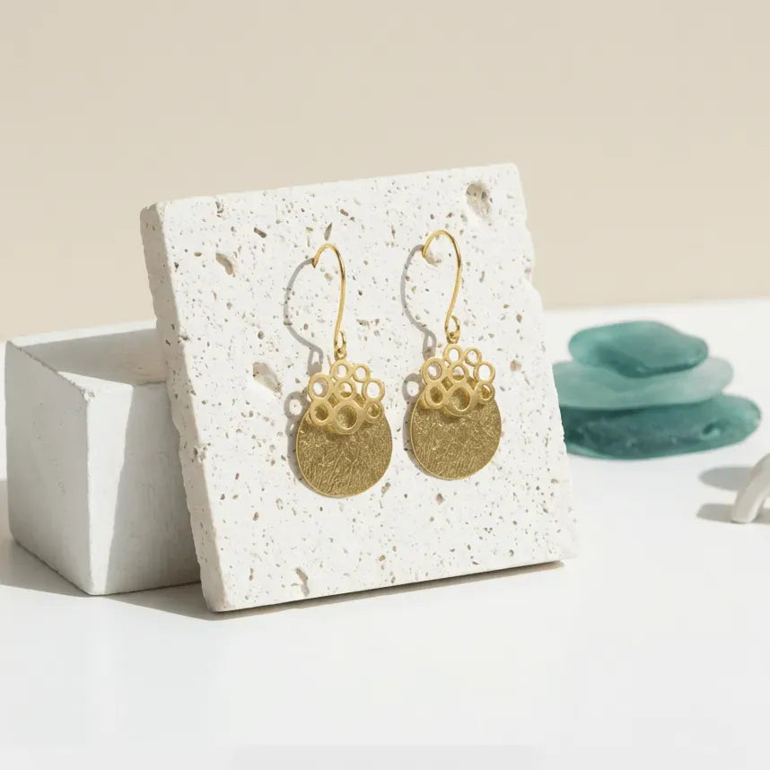Gold earrings on a white card with a beige background