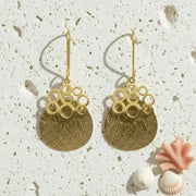 Gold earrings with bubble design on a textured surface with shells.