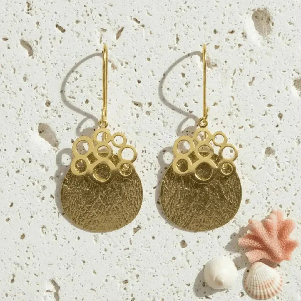 Gold earrings with bubble design on a textured surface with shells.