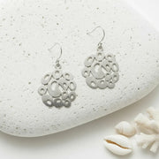 Silver earrings on a textured white stone with shells and coral