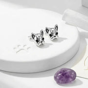 Silver bulldog-shaped earrings on a white stand with a purple stone in the background