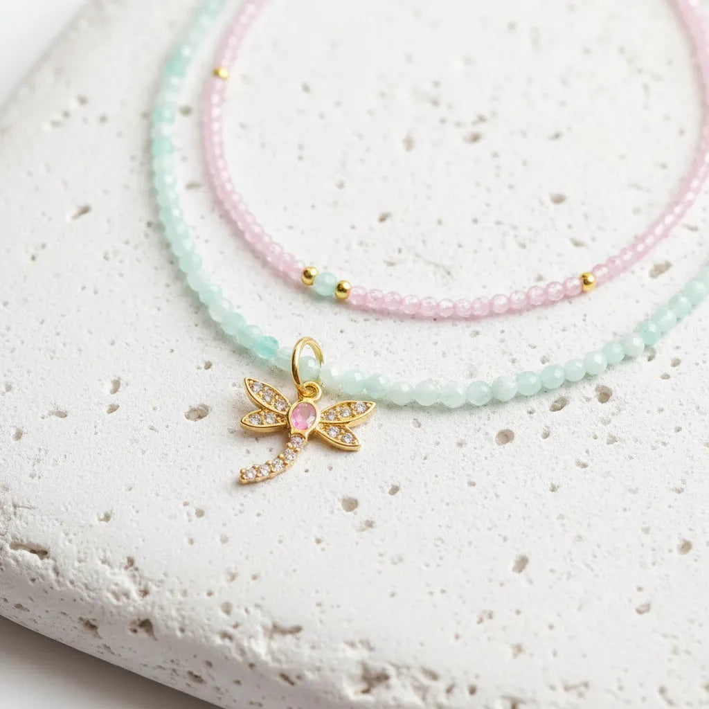 Necklace with a gold dragonfly charm featuring a pink center on a light gray background