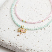 Necklace with a gold dragonfly charm featuring a pink center on a light gray background