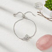 Silver bracelet with butterfly charm on a white surface with a pink stone and plant in the background