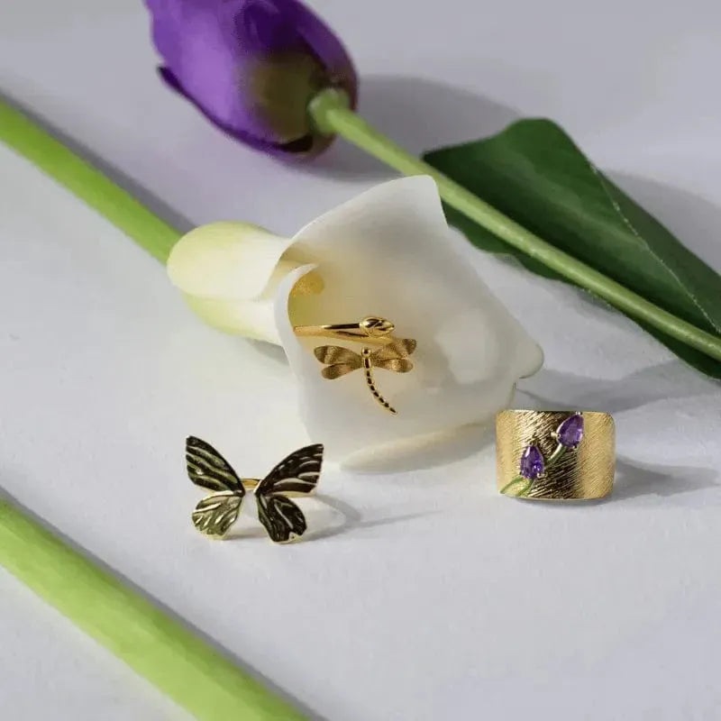 Gold butterfly earrings and ring with a purple flower on a white surface