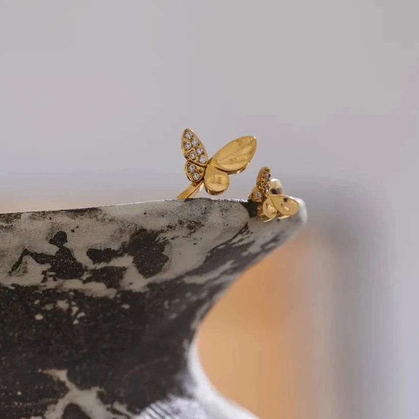 Gold butterfly earrings on a marble surface with a neutral background