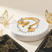 Gold butterfly-shaped ring on a white dish with gold butterflies around
