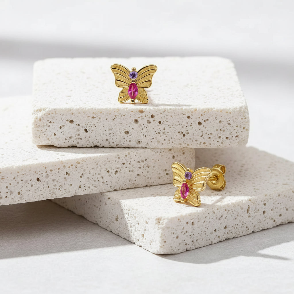 Gold butterfly earrings with pink gemstones on a light white background