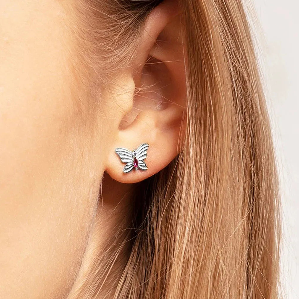 Butterfly-shaped earring with a red gemstone worn by a person with blonde hair.