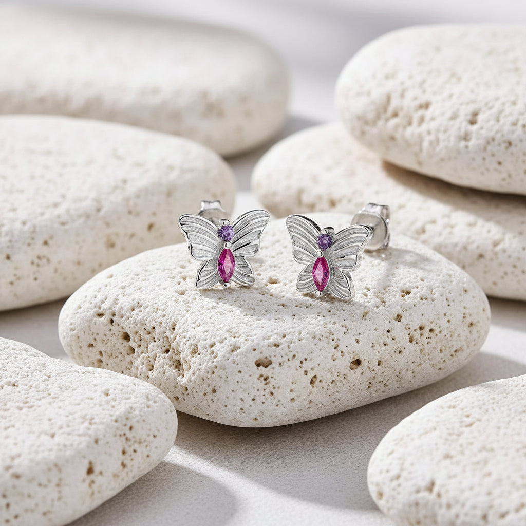 Butterfly-shaped earrings with pink gemstones on a light gray background 