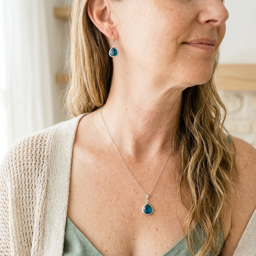 Woman wearing a silver Capri blue Mini Pebble necklace and matching earrings in faceted glass