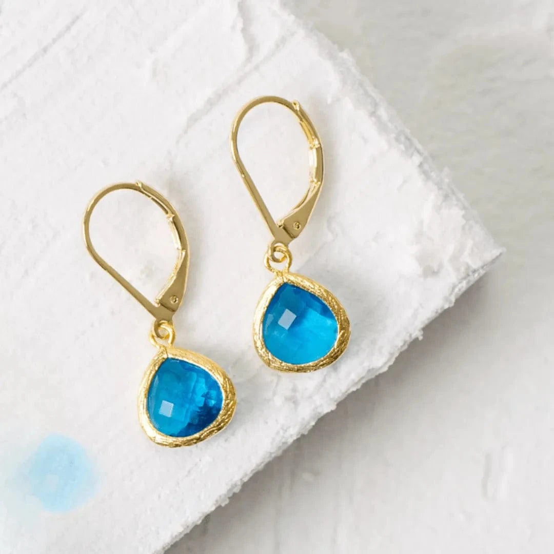 Gold earrings with blue teardrop-shaped gemstones on a white towel.
