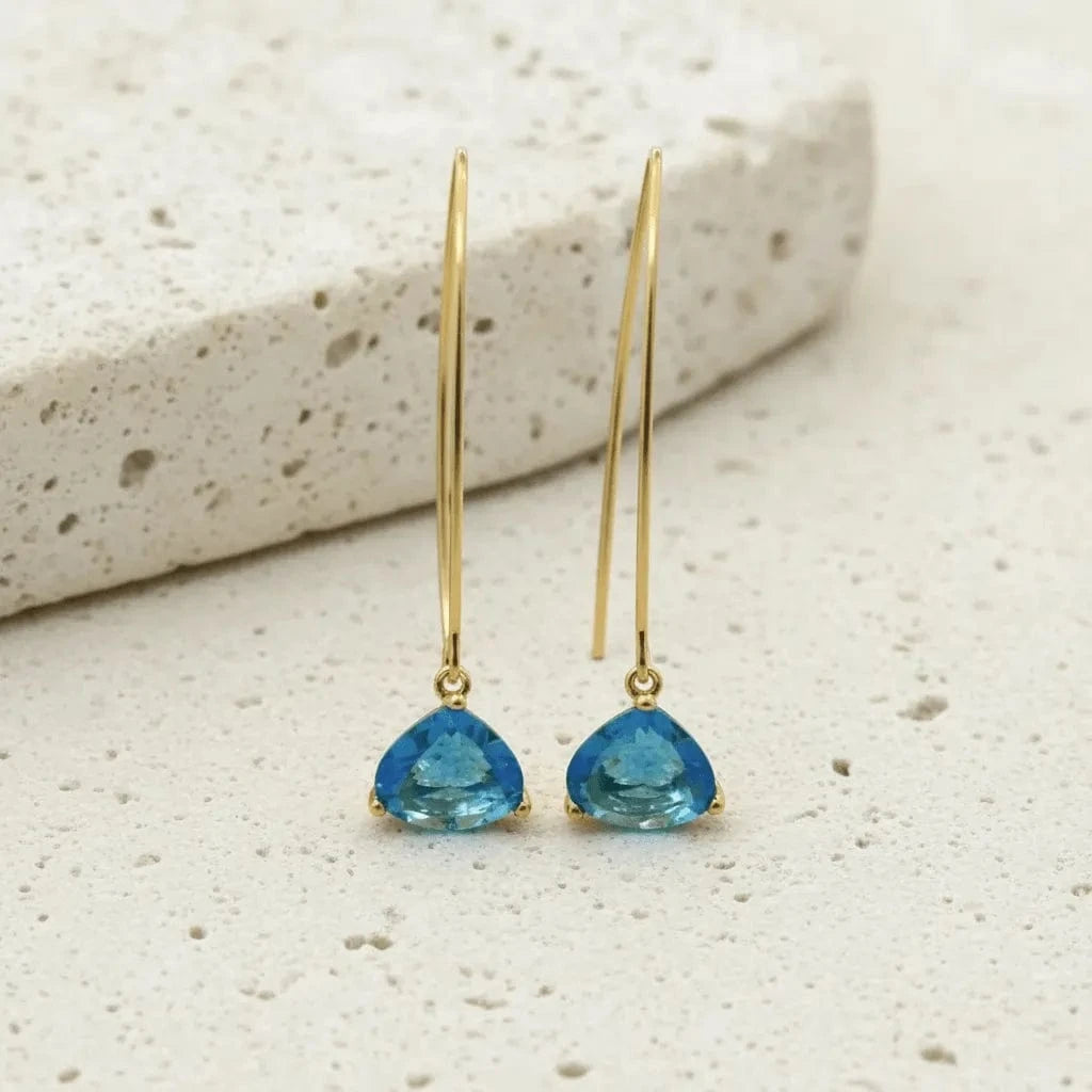 Gold earrings with blue teardrop stones on a beige surface