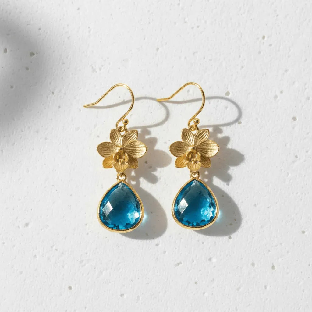 Gold earrings with blue teardrop stones on a light gray background