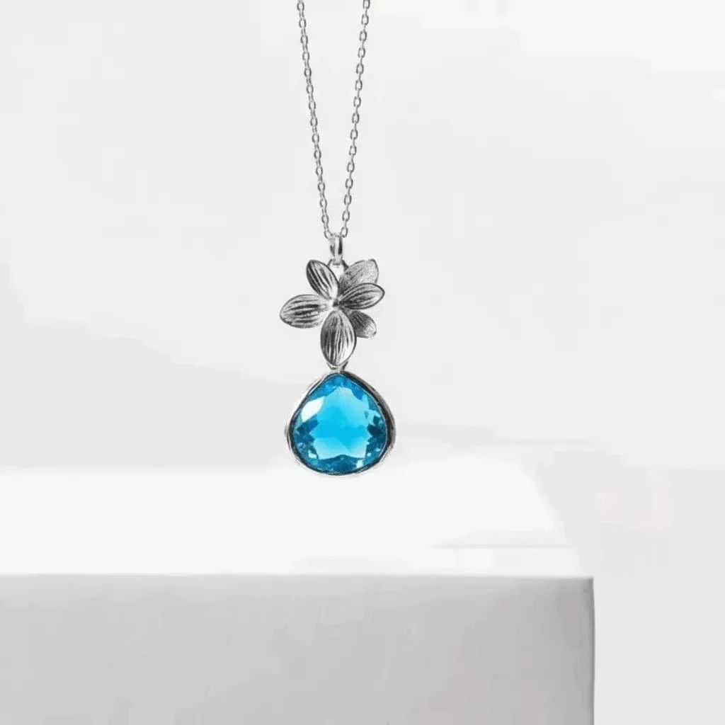 Necklace with a blue teardrop pendant and silver flower design on a white background