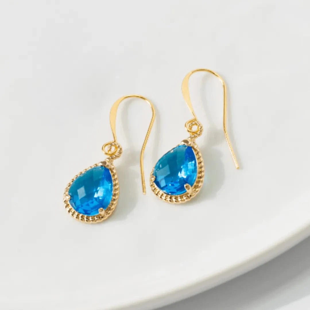 Gold earrings with blue teardrop-shaped gemstones on a white surface