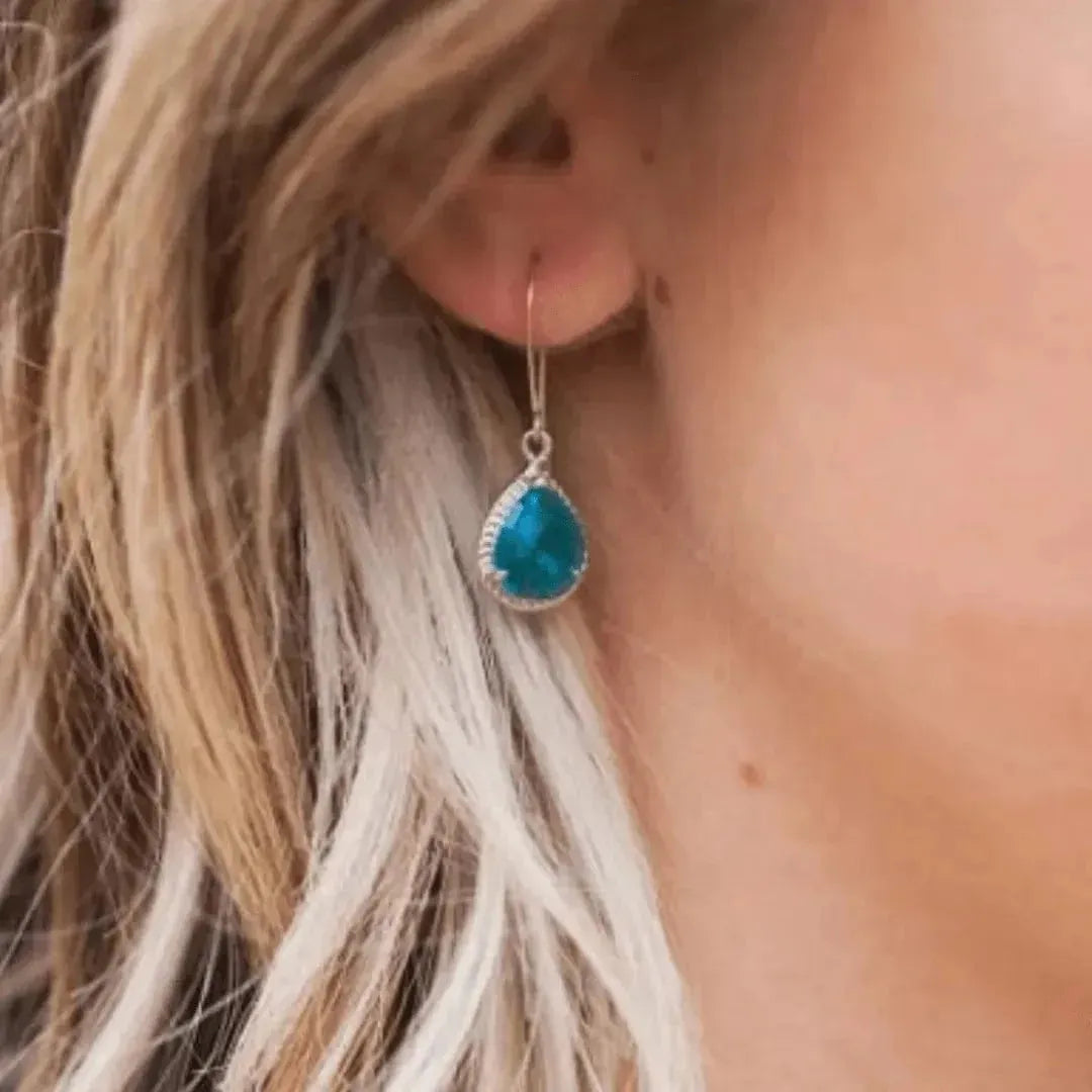 Teardrop-shaped blue earring worn by a person with blonde hair.