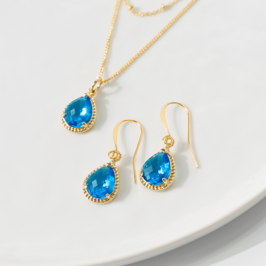 Gold jewelry set with blue teardrop stones on a white plate