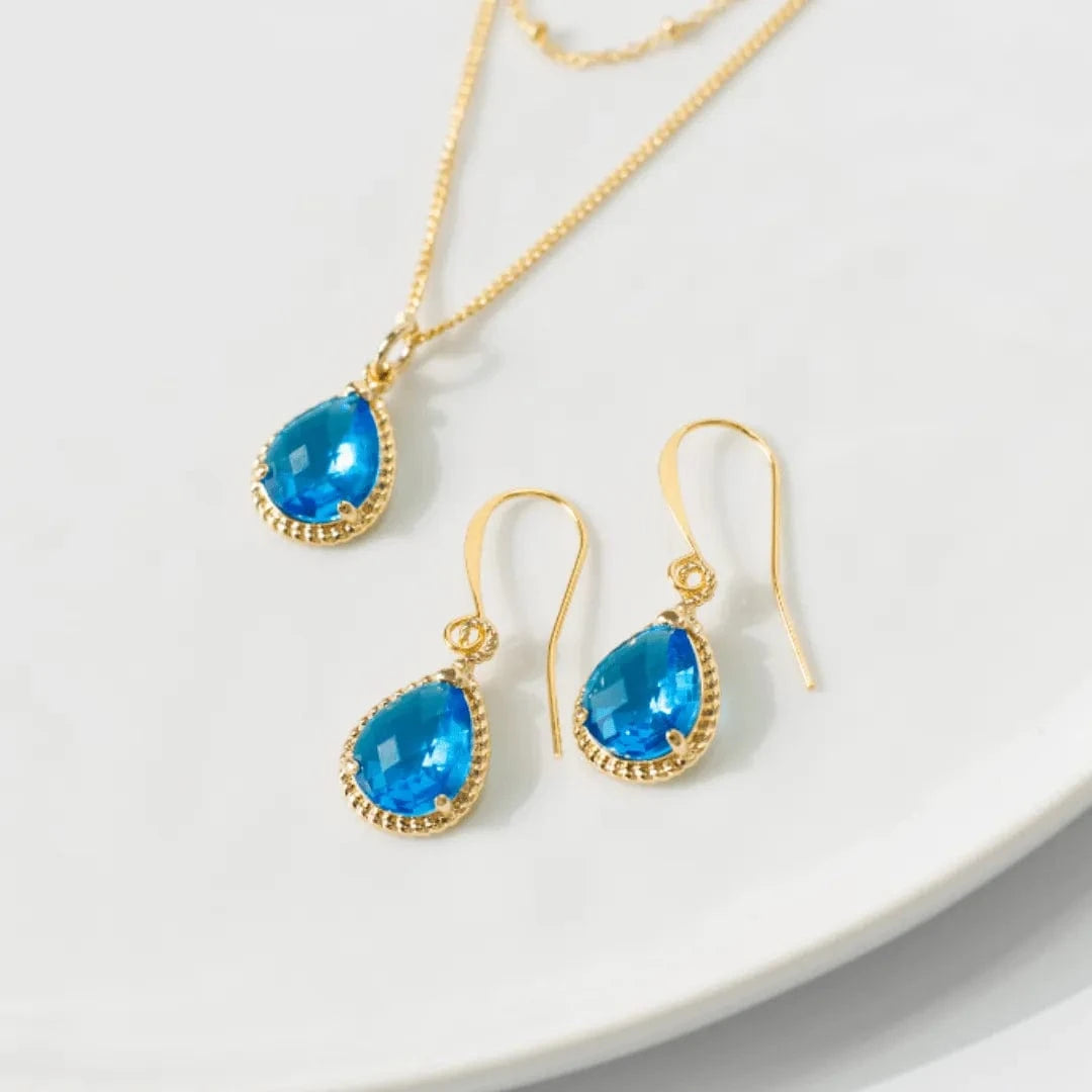 Gold jewelry set with blue teardrop stones on a white plate