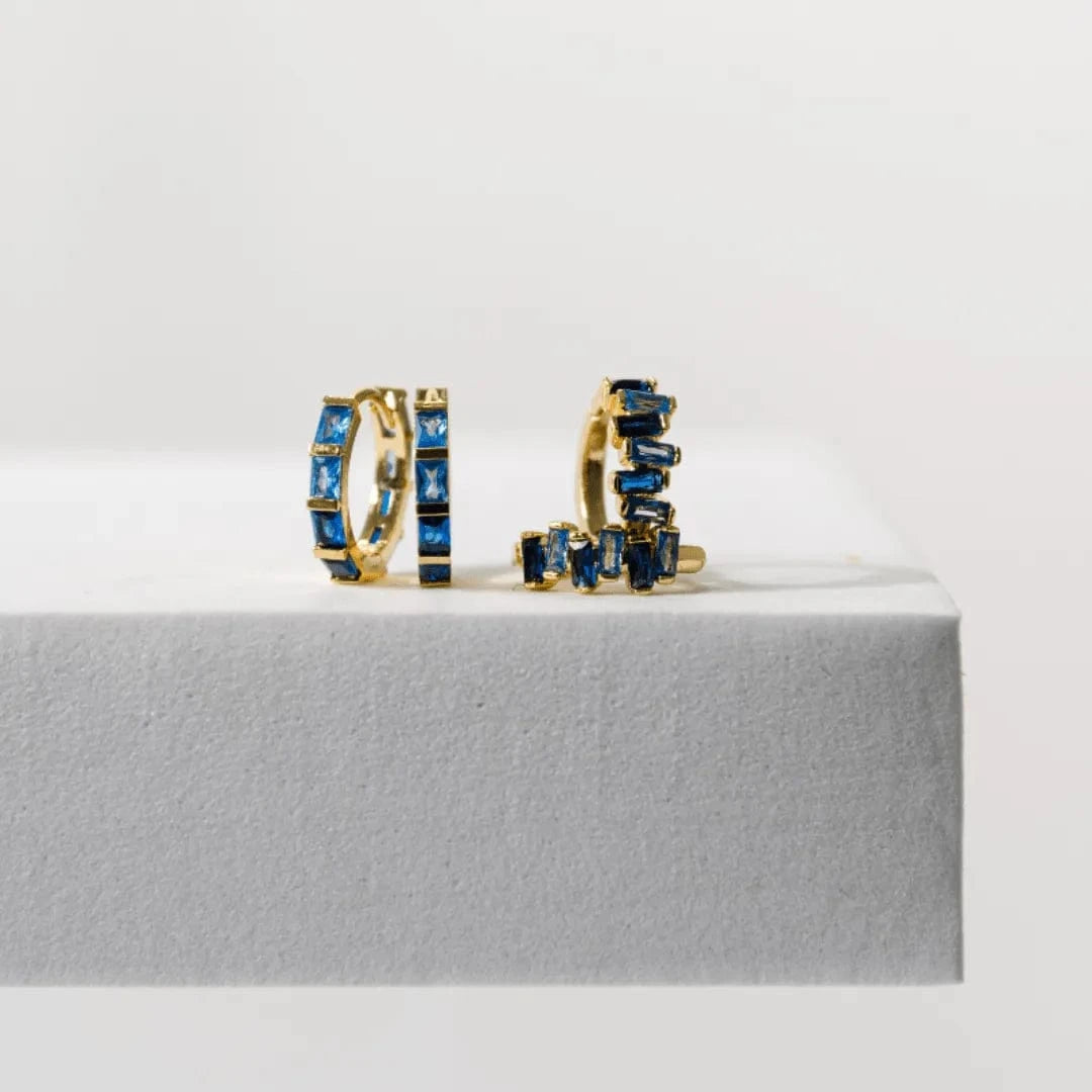 Gold hoop earrings with blue gemstones on a gray surface