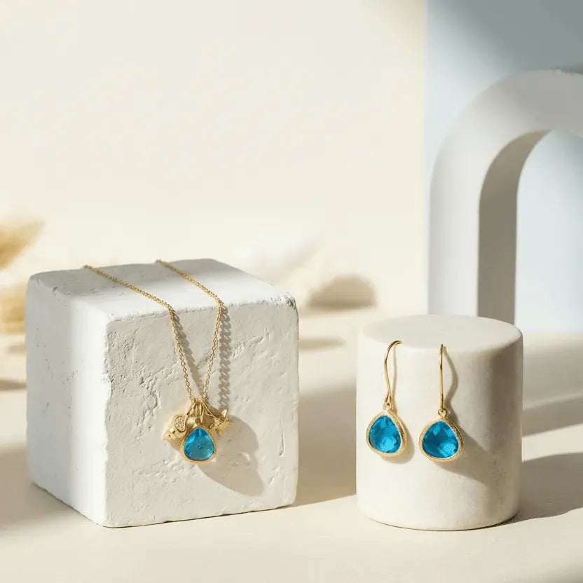 Gold necklaces with blue gemstones on white cubes against a light background