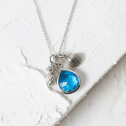 Necklace with blue pendant and shell charm on a white textured surface