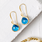 Gold earrings with blue gemstones on a white surface