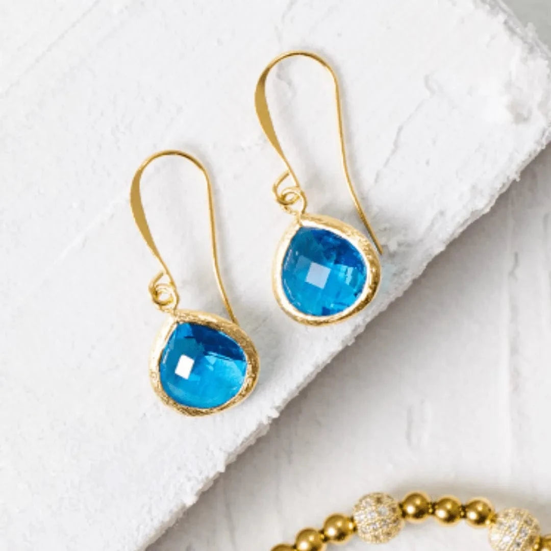 Gold earrings with blue gemstones on a white surface