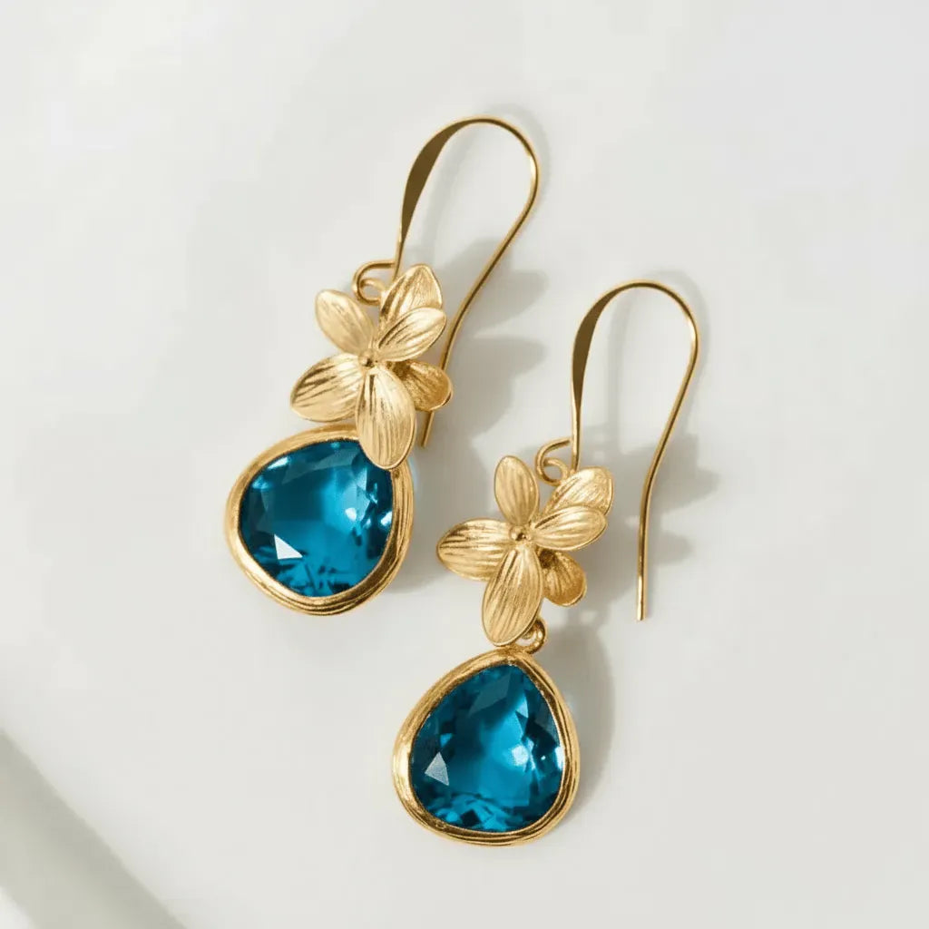 Gold earrings with blue teardrop stones on a light background